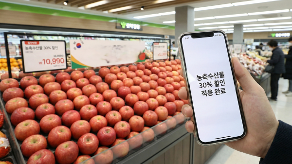 대형마트 과일 매대 앞에서 스마트폰 앱으로 할인 쿠폰을 확인하는 모습